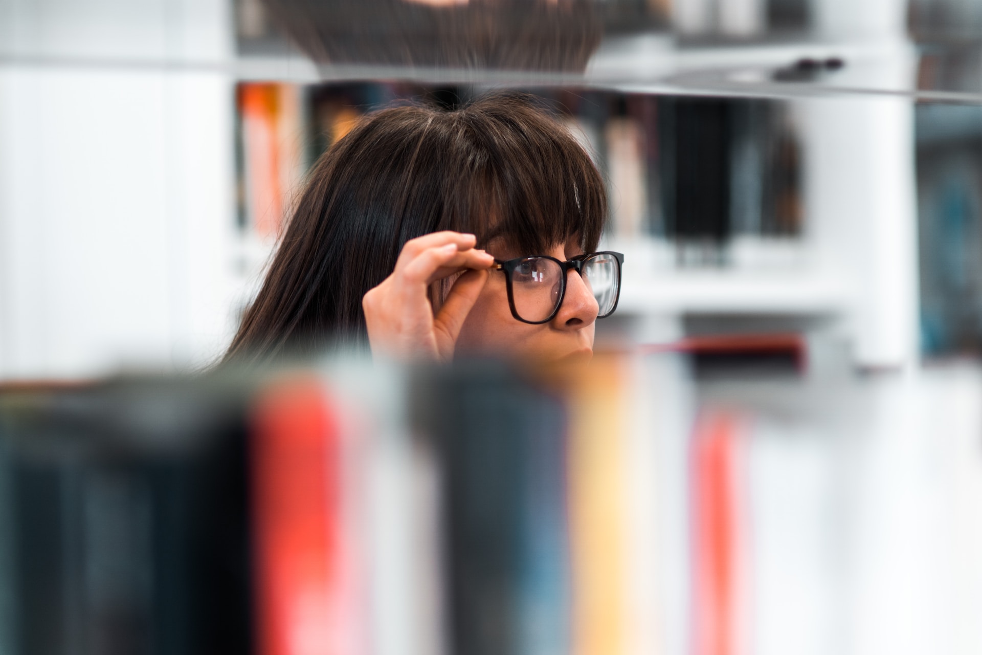 woman peering over glasses surrounded  by books